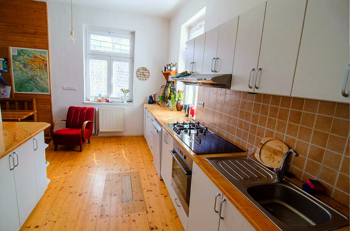 Velká společná kuchyň s bílou linkou a oknem do zahrady
